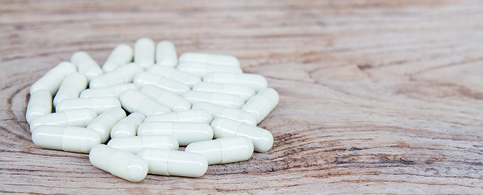 Белые капсулы лекарств на деревянной поверхности